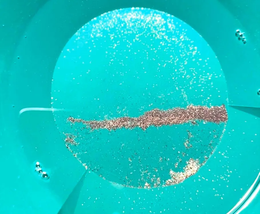 Goldpartikel in blauer Pfanne, Wasserumgebung.