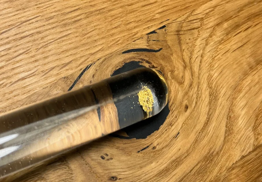 Glass tube with gold particles on wooden surface.