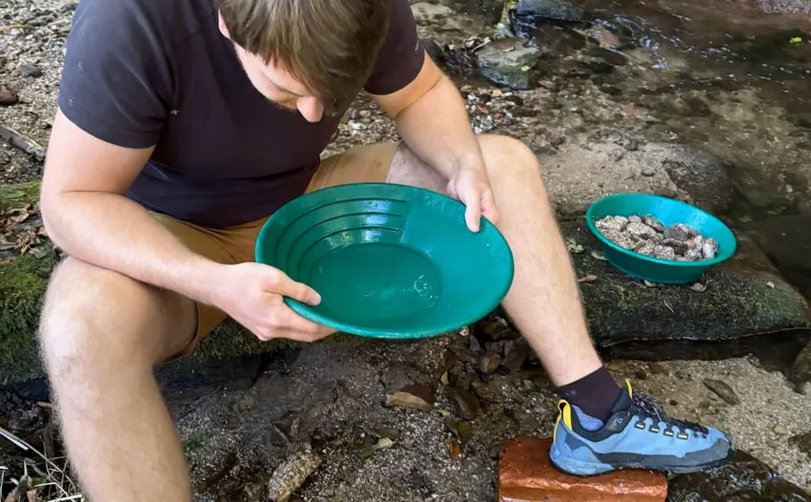 Person panning for gold by a stream.