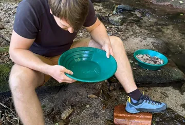 Man panning for gold by a stream.