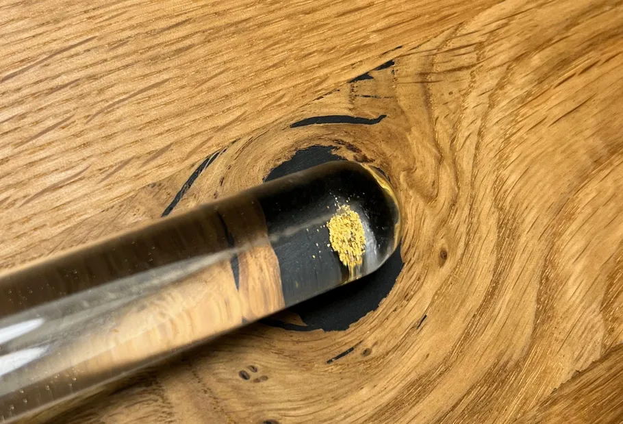 Glass vial with gold powder on wood surface.