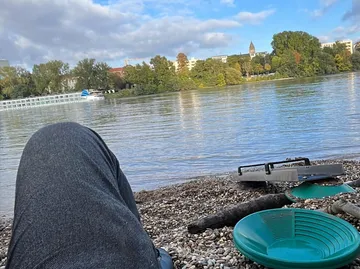 Person entspannt am Flussufer mit Goldpfannen.