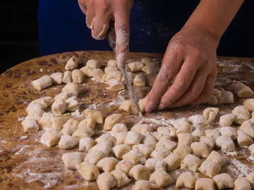 Hands cut gnocchi on a floured wooden plate.