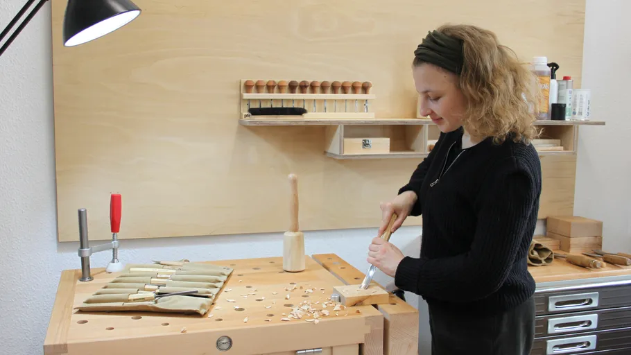 Frau schnitzt Holz an einer Werkbank.