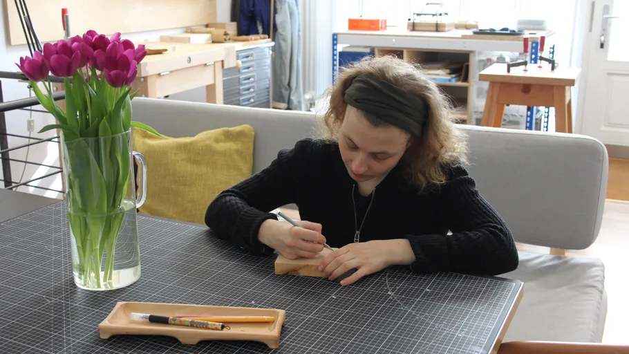 Person engraving wood at desk, room with flowers.
