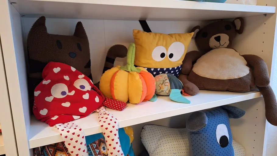 Stuffed toys on white shelf, various shapes.