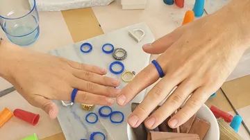 Hands wearing blue rings, surrounded by tools.