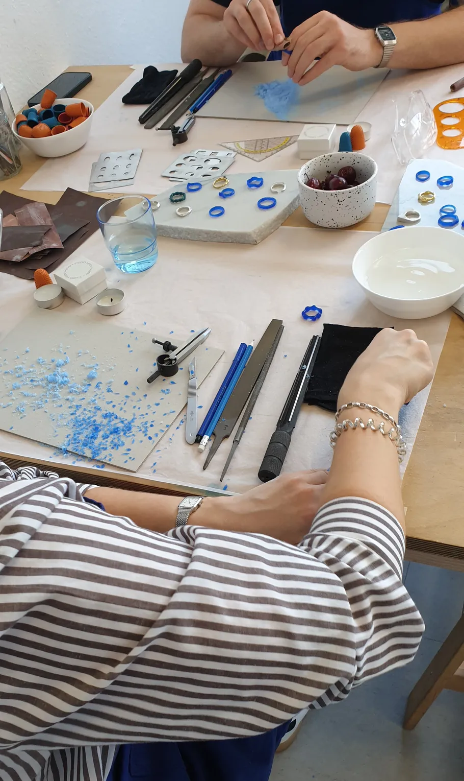 Personen fertigen Schmuck mit Werkzeugen am Tisch.