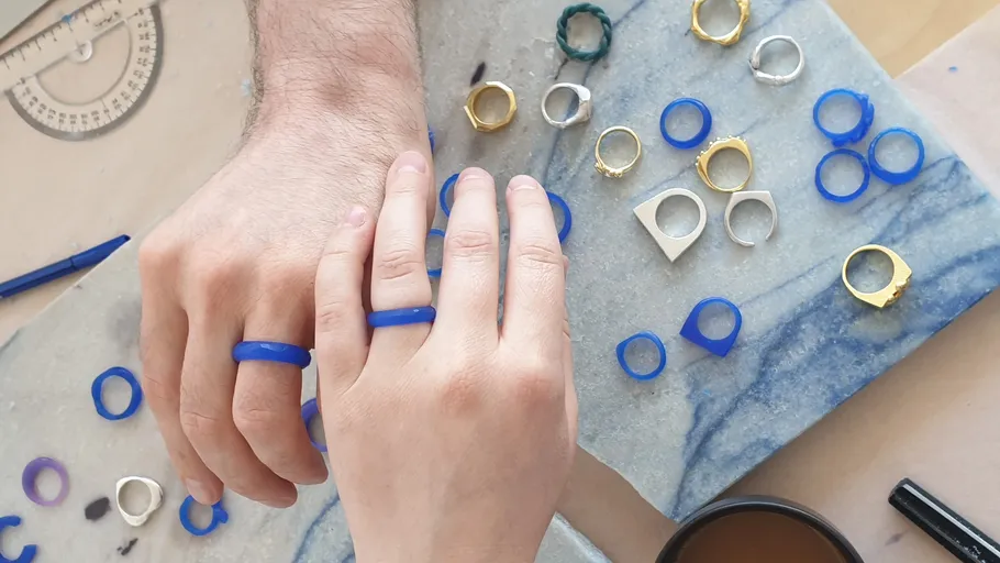 Hände mit blauen Ringen, umgeben von Formen.