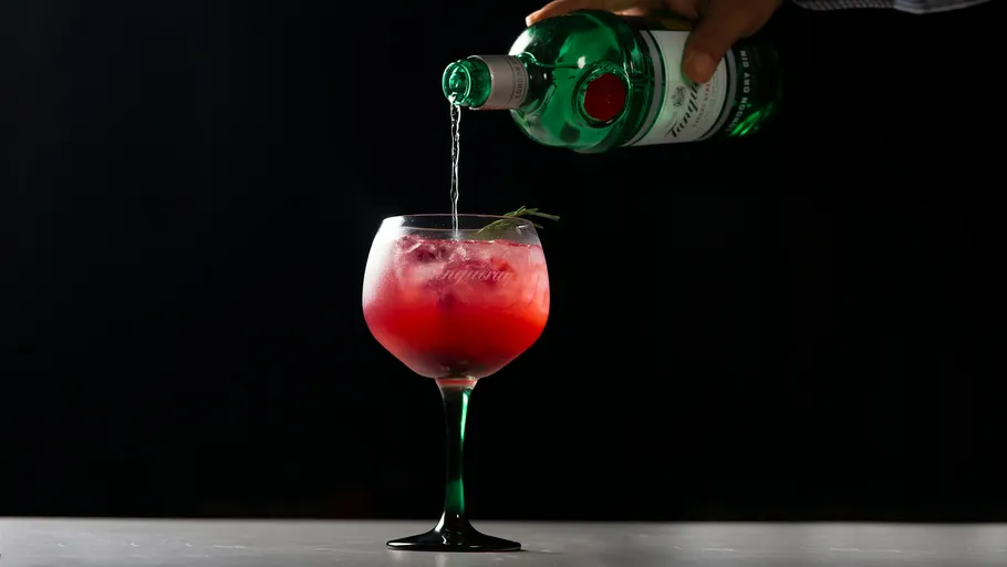 Green bottle pouring drink into red cocktail glass.