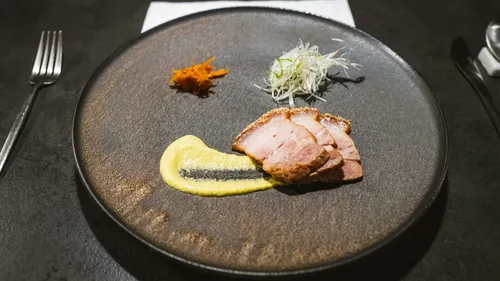 Sliced duck breast on dark plate, gourmet presentation.