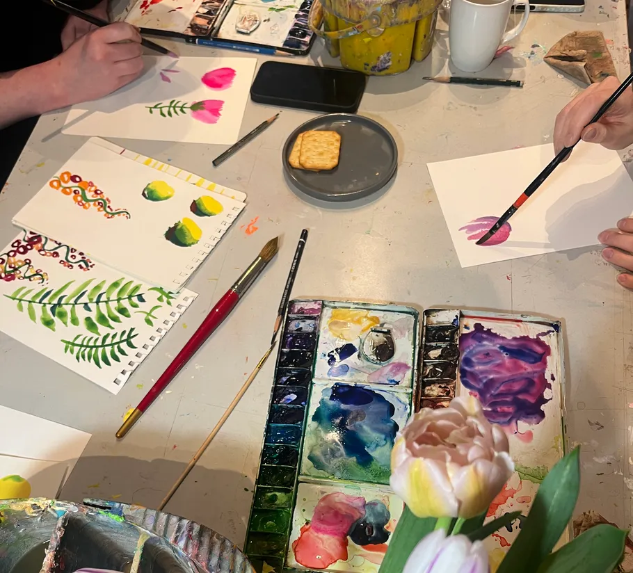 Menschen malen Blumen an einem Tisch.