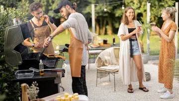 Zwei Männer grillen, zwei Frauen plaudern daneben.