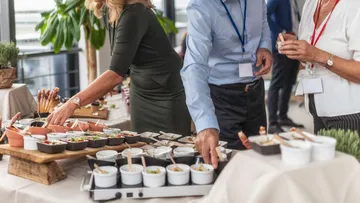 Personen wählen Speisen von einem Buffet bei einer Veranstaltung.