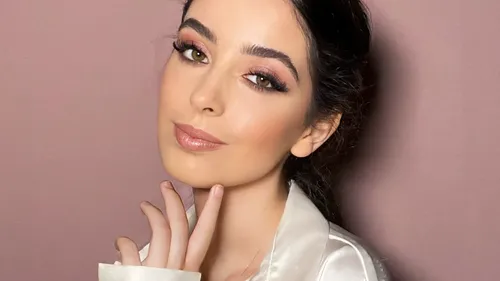 Woman posing thoughtfully against pink background.