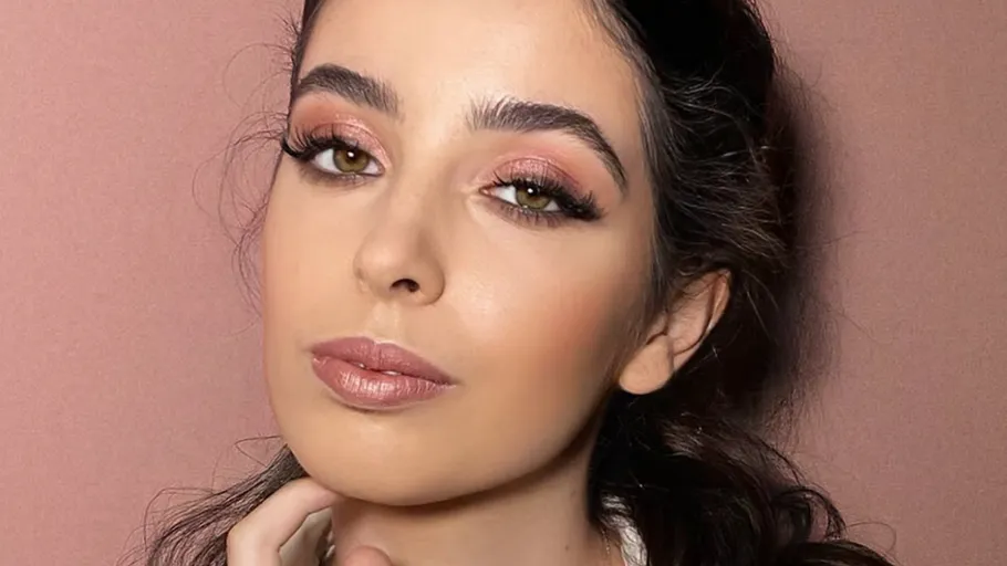 Frau mit Make-up posiert vor rosa Hintergrund.