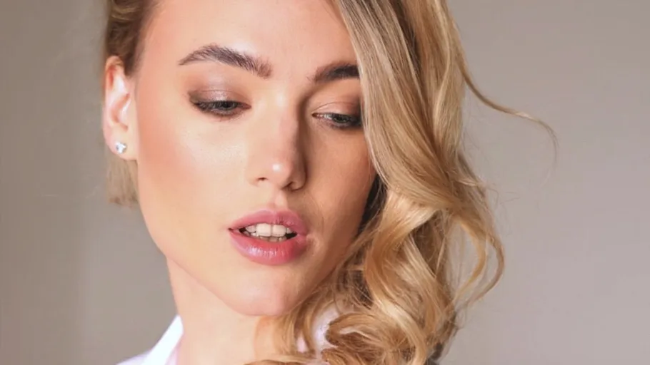 Frau mit blondem Haar schaut nach unten, neutraler Hintergrund.