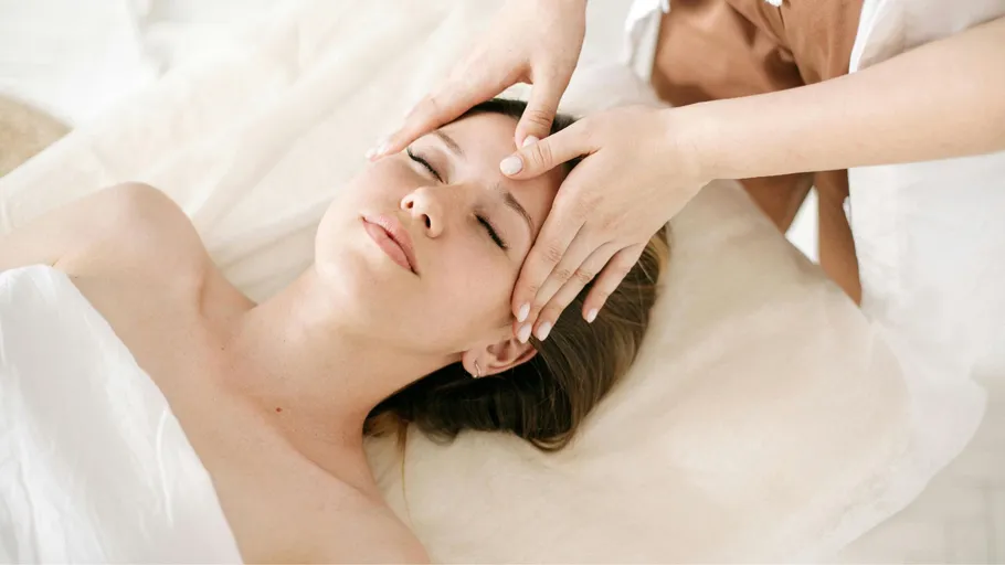 Frau erhält Gesichtsmassage auf einem Bett.