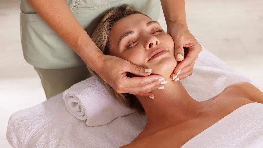 Woman receiving facial massage on cushioned table.