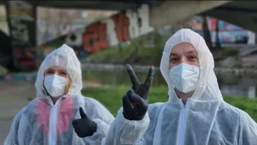 Two people in protective suits under a bridge.