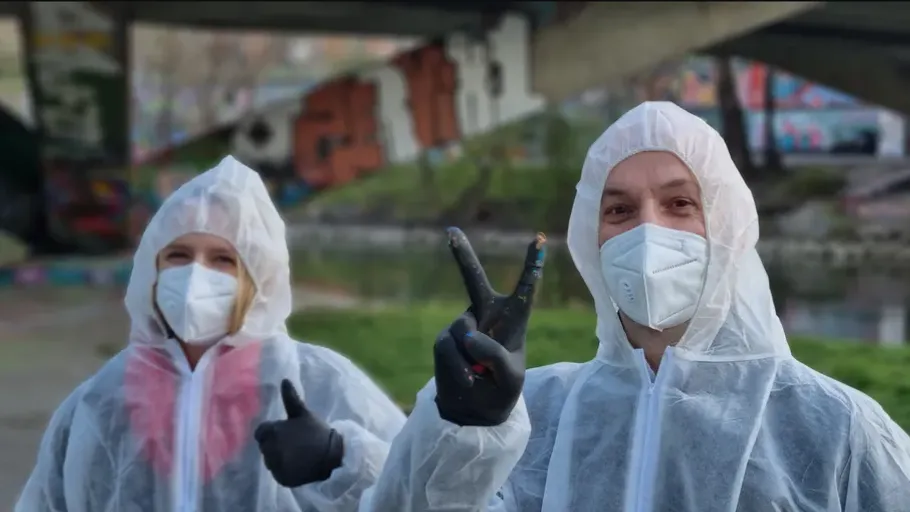Two people in protective suits under a bridge.