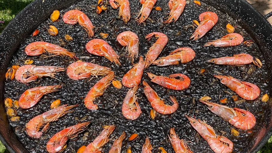 Meeresfrüchte-Paella mit Garnelen und schwarzem Reis im Freien.