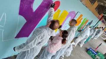 Personen malen Graffiti an eine Wand, in Schutzanzügen.