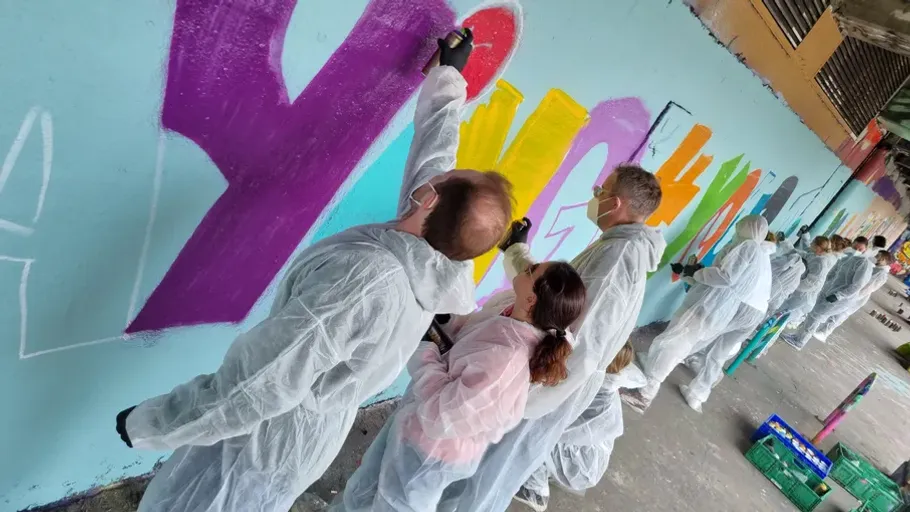 People painting graffiti on a wall, wearing coveralls.