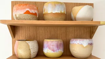 Bunte Keramiktöpfe auf einem Holzregal.