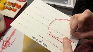 Hände nähen Zahlen auf Papier mit Nadel.
