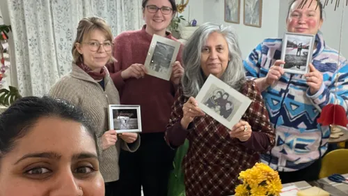 Five women holding framed photos, indoors.