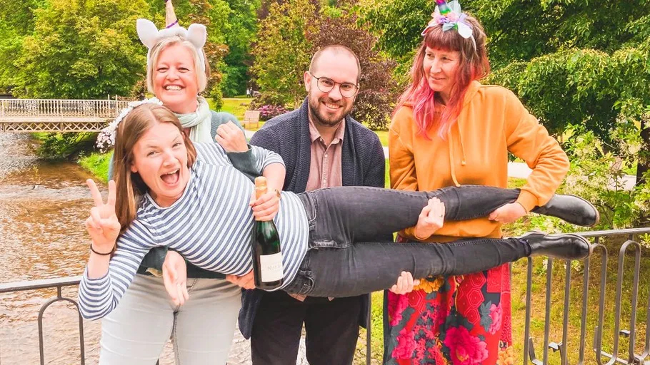 Group holding a woman by a river.