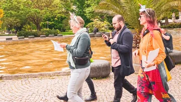 Drei Personen gehen in einem Park nahe einem Teich.