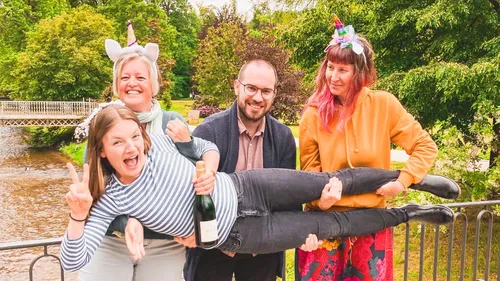 Four people cheerfully holding another in park.