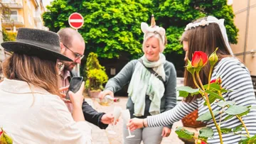 Menschen feiern draußen mit Getränken und Rosen.