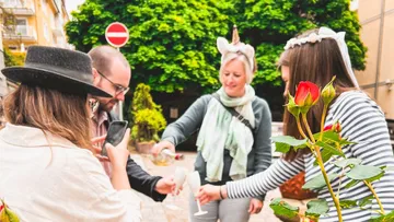 Gruppe teilt Getränke draußen bei Rosenstrauch.