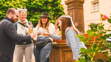 Gruppe feiert im Freien, lachend bei Brunnen.