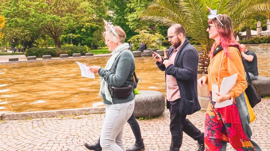 Drei Personen gehen mit Papieren am Brunnen vorbei.
