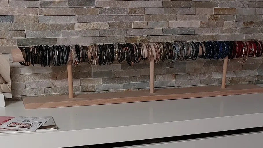 Armbänder auf Holzständer, Steinwand im Hintergrund.