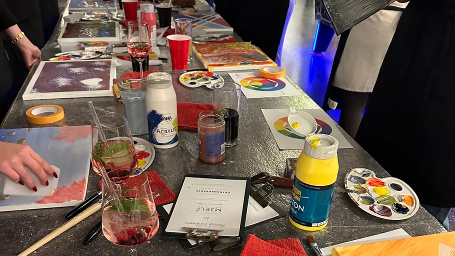 Paint supplies and drinks on table with people.