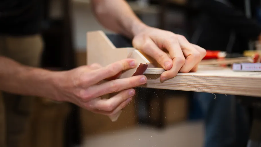 Hands sanding wooden edge in workshop.