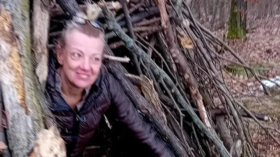 Woman smiling in a wooded stick shelter.
