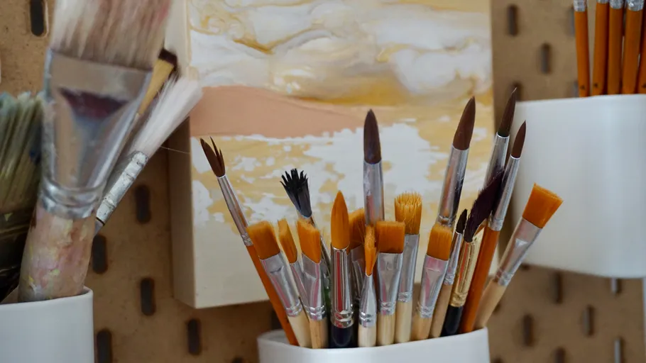 Paintbrushes in holders near unfinished painting.