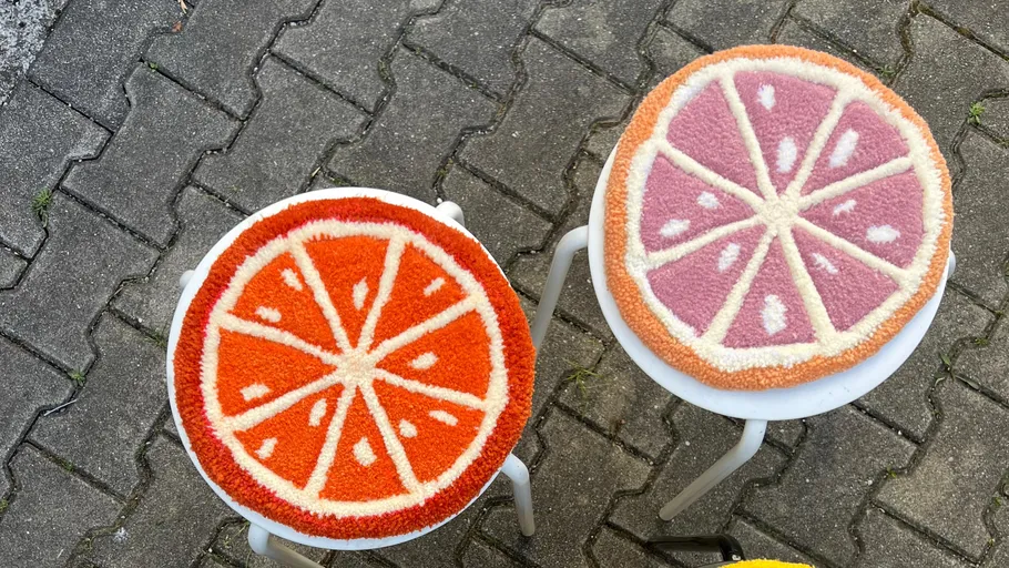 Two fruit-patterned stools on a paved ground.