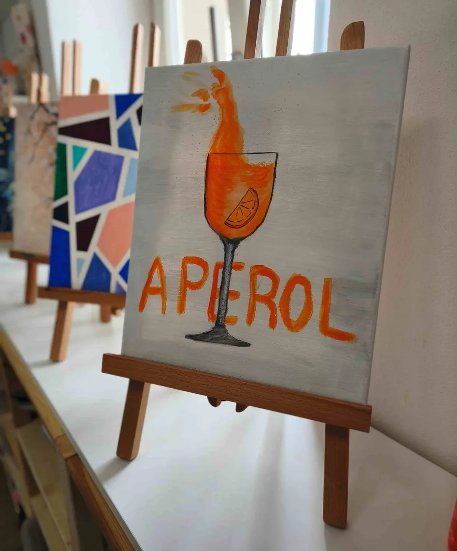Painting of Aperol drink on easel indoors.