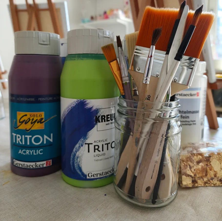 Paintbrushes in jar, acrylic paints beside.