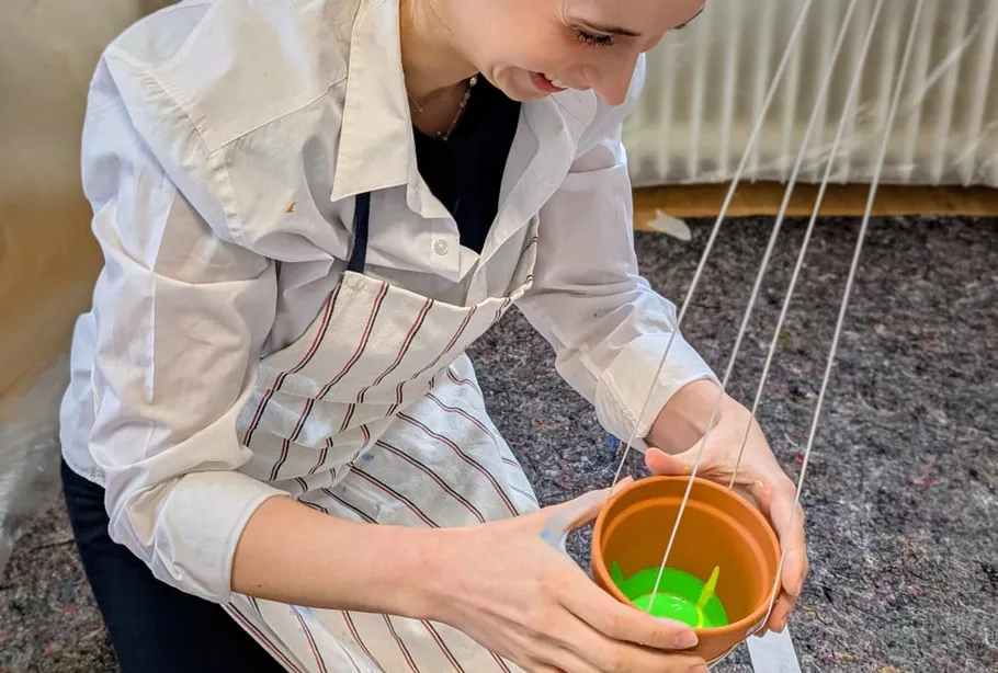 Woman holding plant pot with strings indoors.