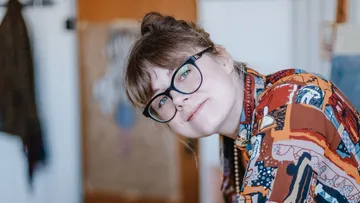 Person mit Brille lächelt, trägt buntes Hemd.