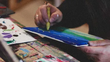 Person painting with crayons on colorful paper.