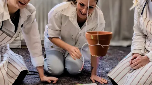 People in aprons crafting with hanging pot.